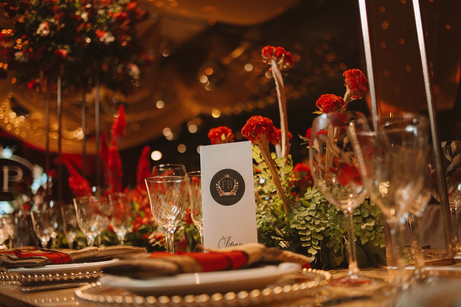 Mesa posta com flores vermelhas, taças de cristal e menu personalizado