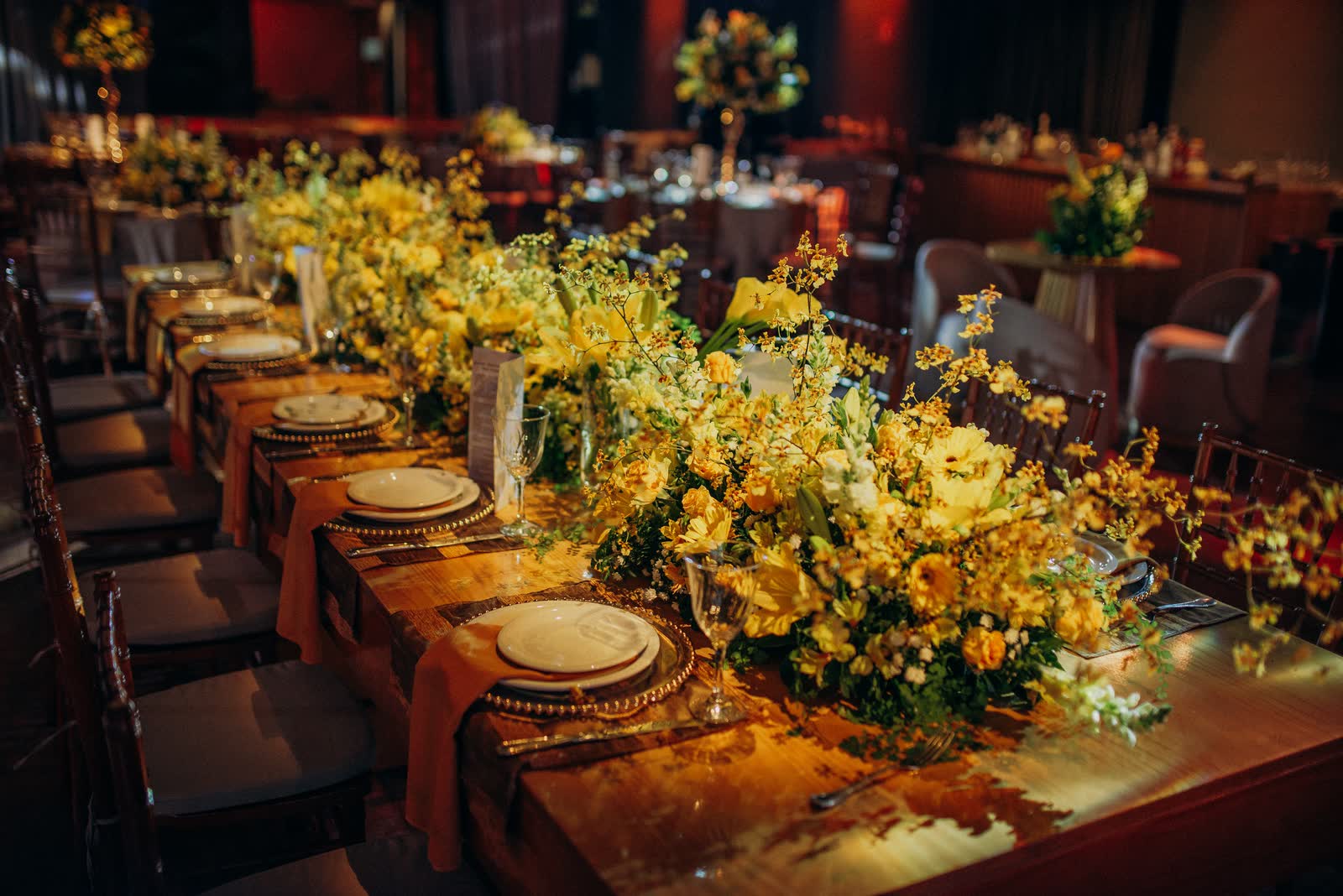 Mesa comprida com arranjos de flores amarelas e sousplats dourados