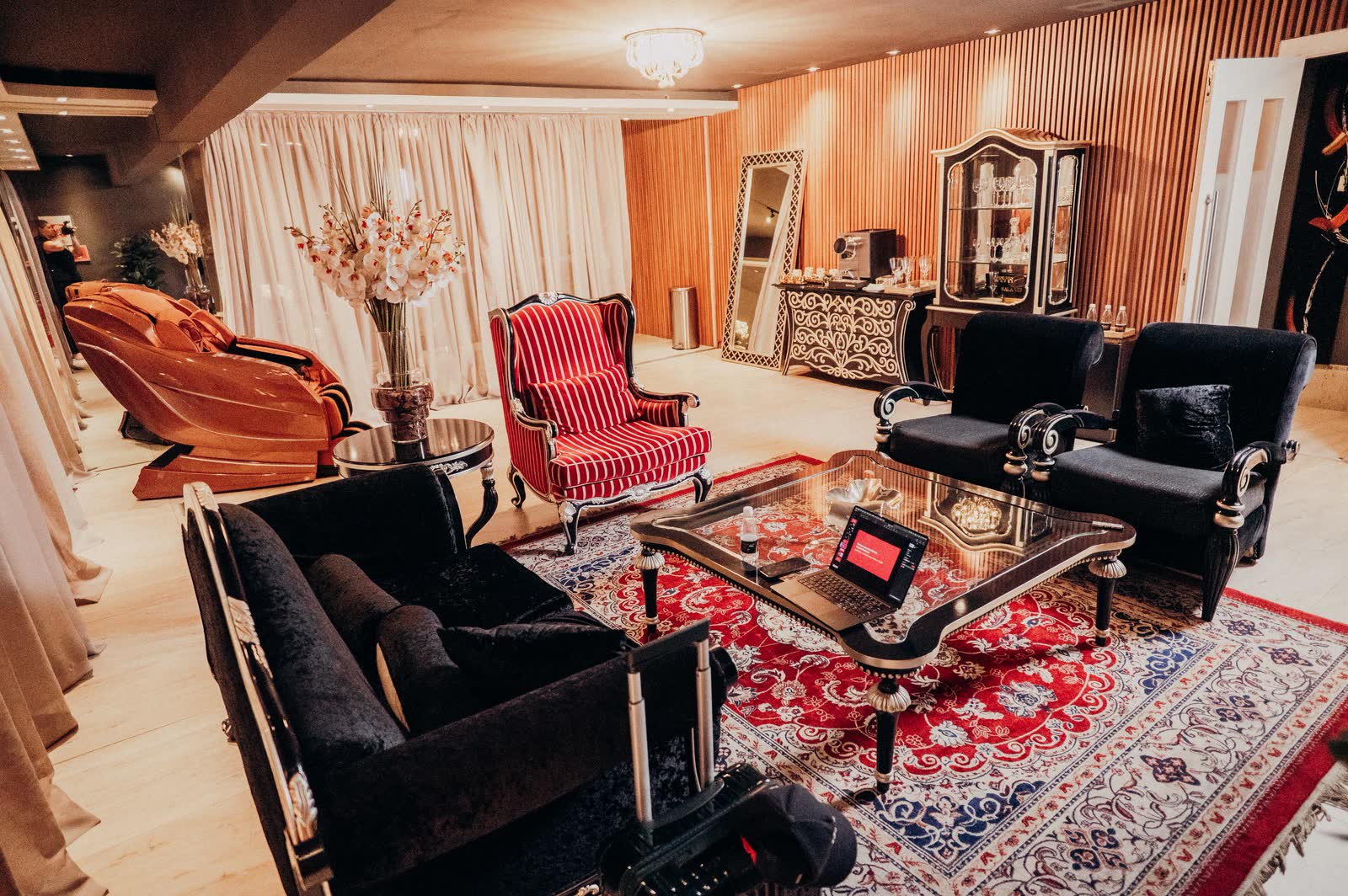 Sala VIP com poltronas listradas, sofás de veludo preto e tapete persa
