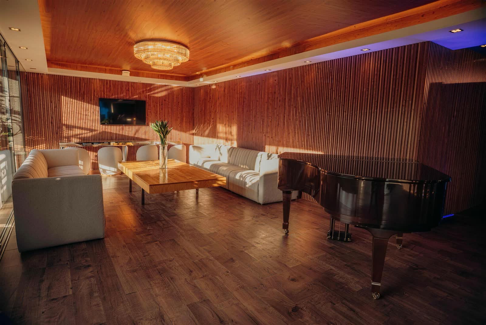 Lounge com sofás brancos, piano de cauda e lustre de cristal