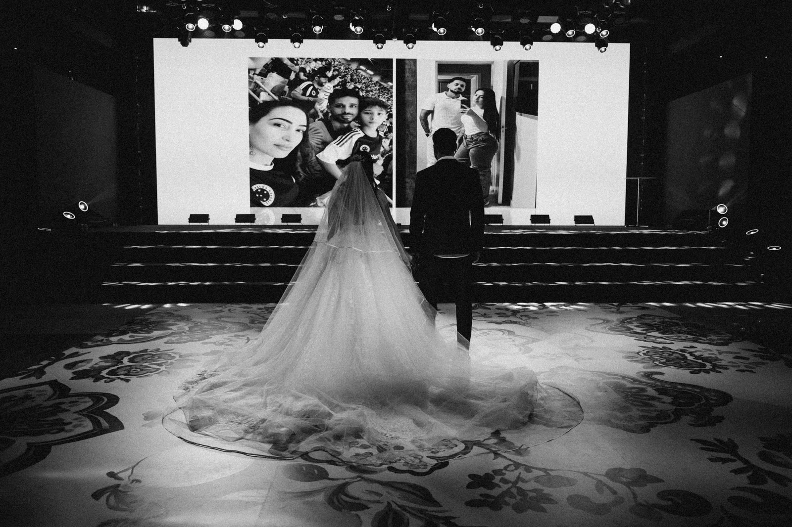 Noivos diante do telão com fotos do casal, em preto e branco