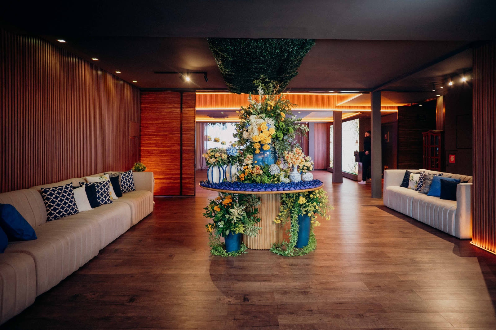 Lounge com sofás brancos e arranjo de flores azuis e amarelas