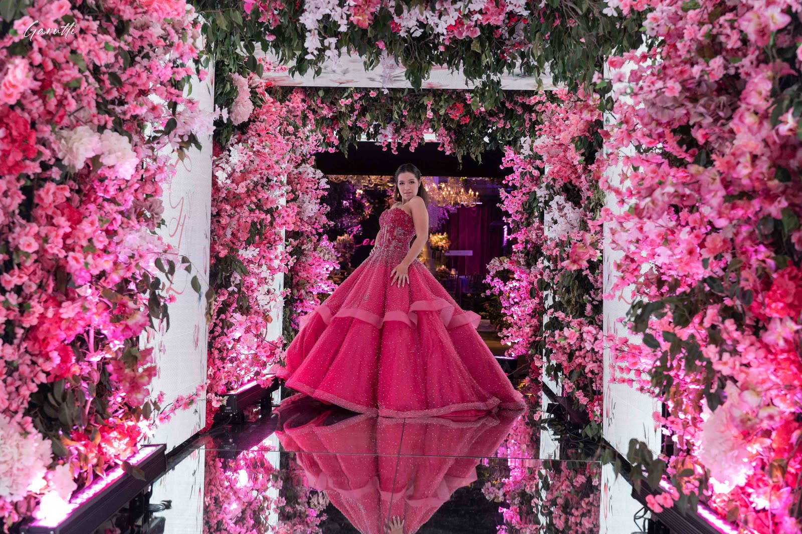 Debutante in a hot-pink gown in a tunnel of flowers
