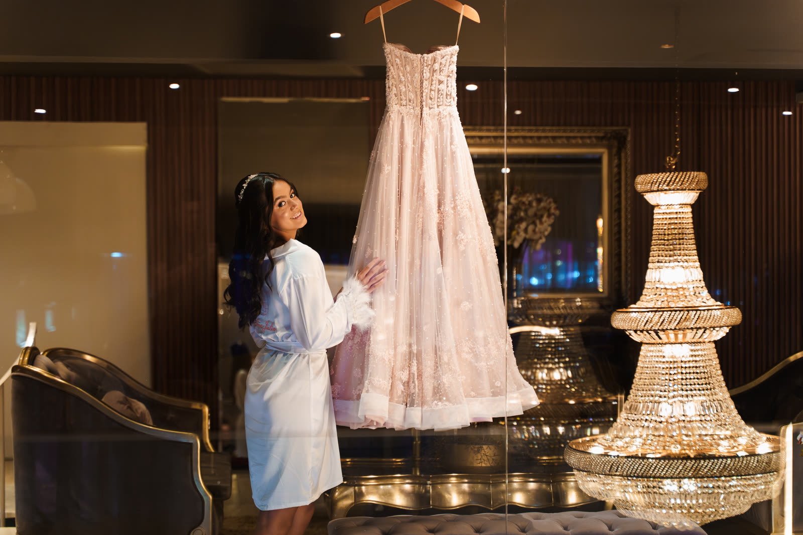 Debutante facing her party gown in the dressing room with a crystal chandelier