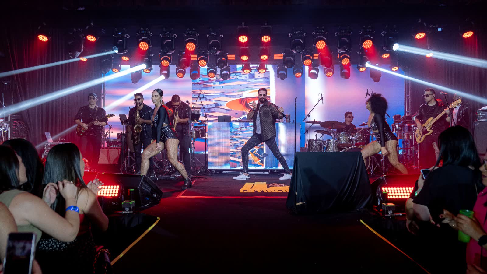 Banda com bailarinas no palco sob luzes vermelhas