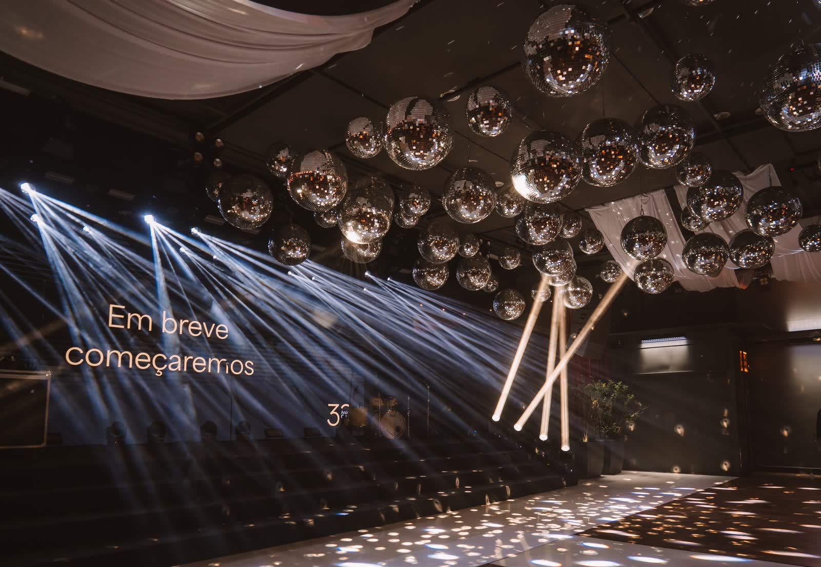 Feixes de luz cênica cruzando o salão sob globos espelhados